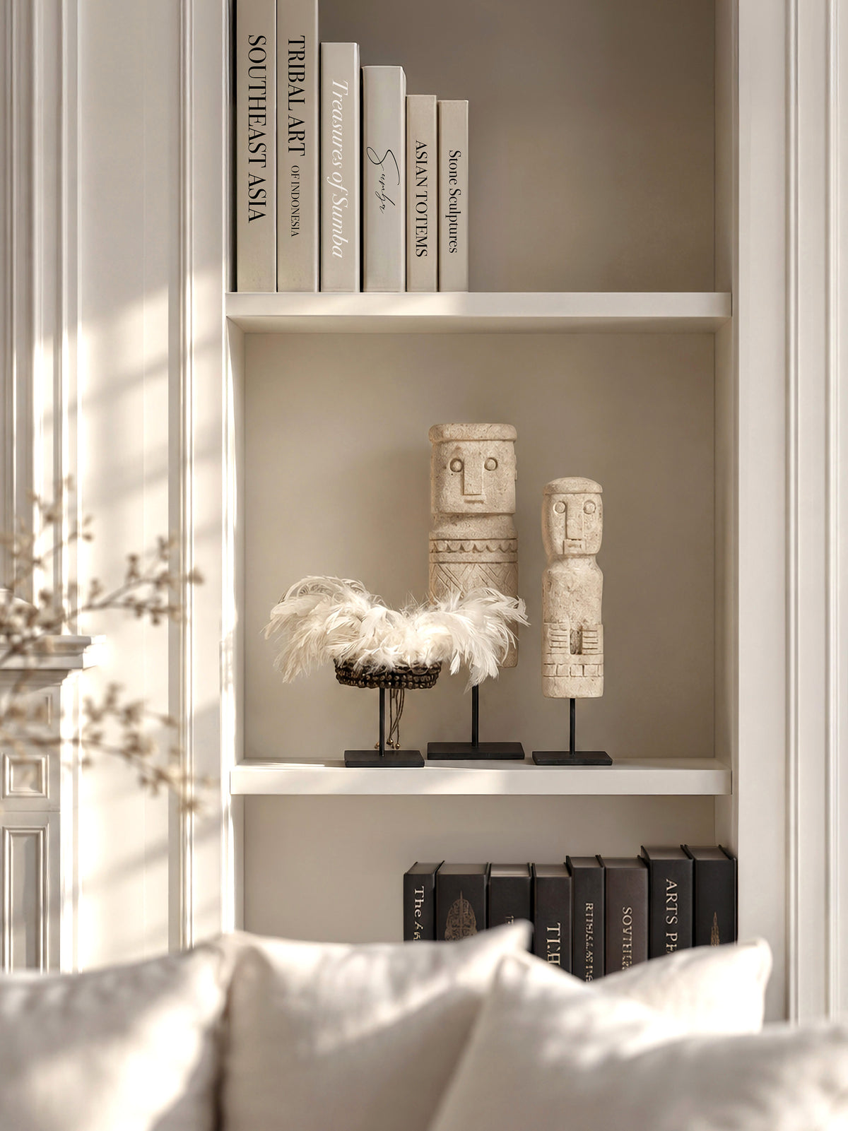 Fortune and Fulfillment set with two Timor limestone totems and a Papua feather-and-shell bracelet on a sunlit white bookshelf