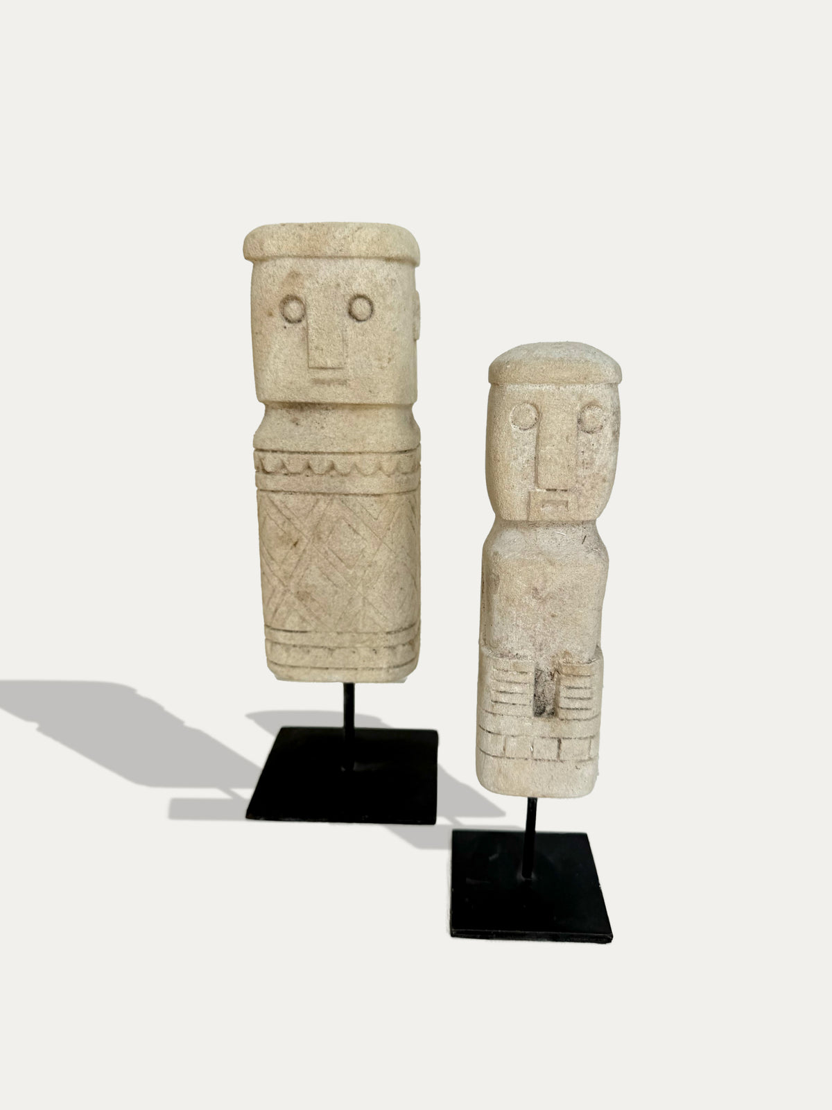 Set of two hand-carved limestone statues from Timor on black metal stands, front view.