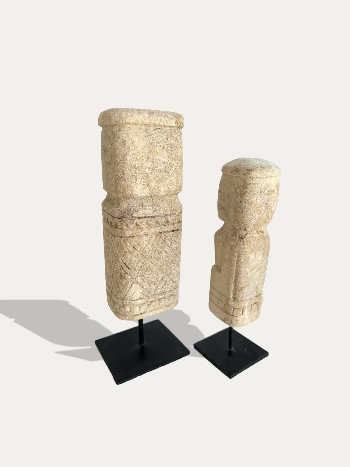 Rear view of two Timor limestone statues on black metal stands, showing carved details and natural stone texture.