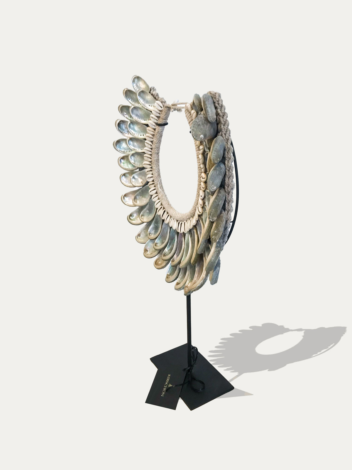 Side view of a Papua abalone shell necklace showing layered shells and natural fibre construction on a black metal stand.