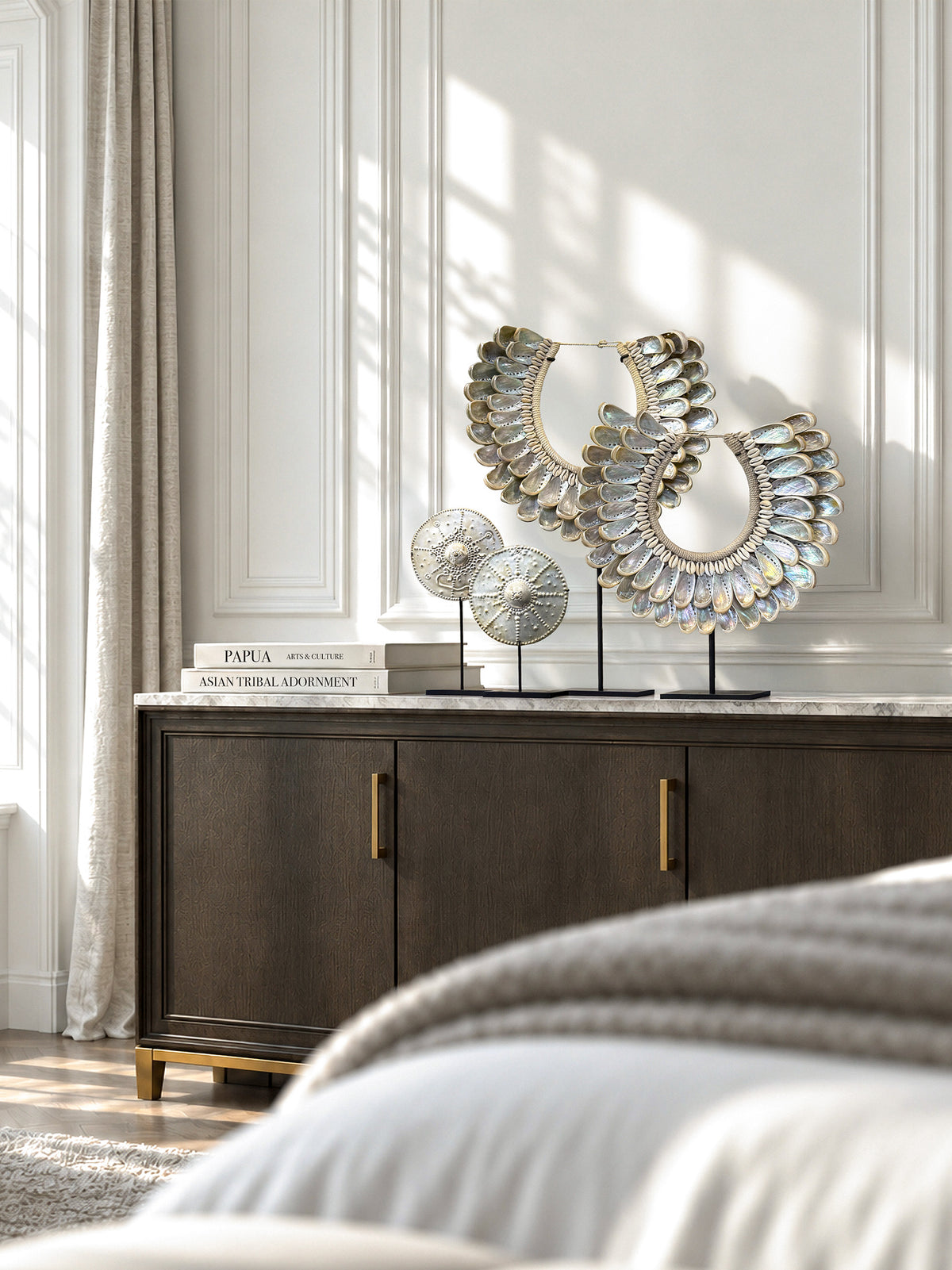 Papua abalone shell necklaces and Timor brass pectoral plates on black stands, displayed on a bedroom cabinet in Treasures of the Tides.
