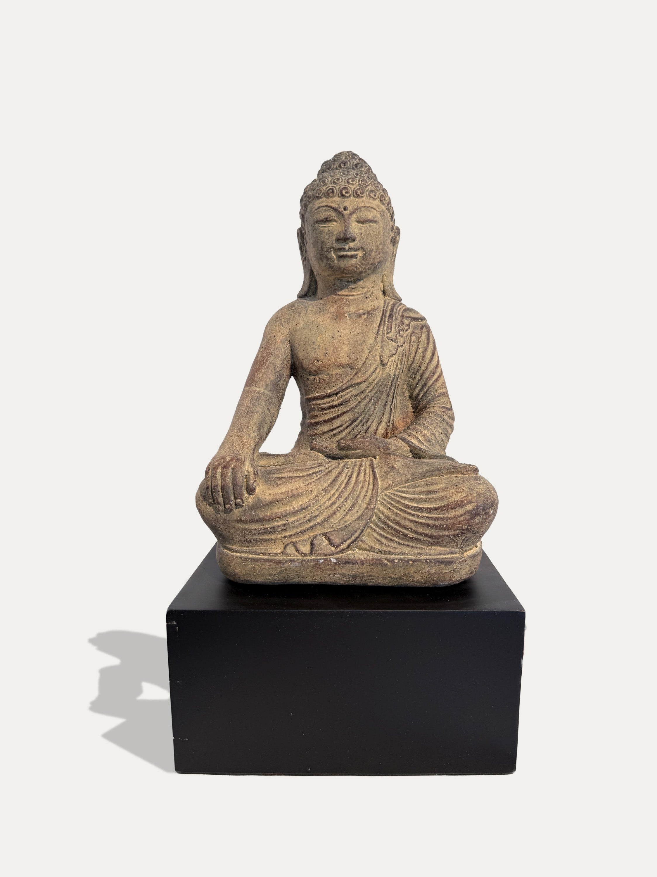 A seated Buddha statue in a natural stone finish, displayed on a black rectangular pedestal against a light gray background.